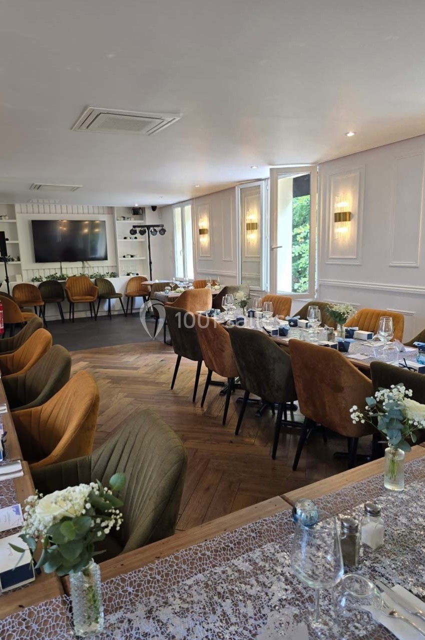 Salle de réception lumineuse avec tables dressées, chaises colorées et décorations florales, vue sur un écran mural.