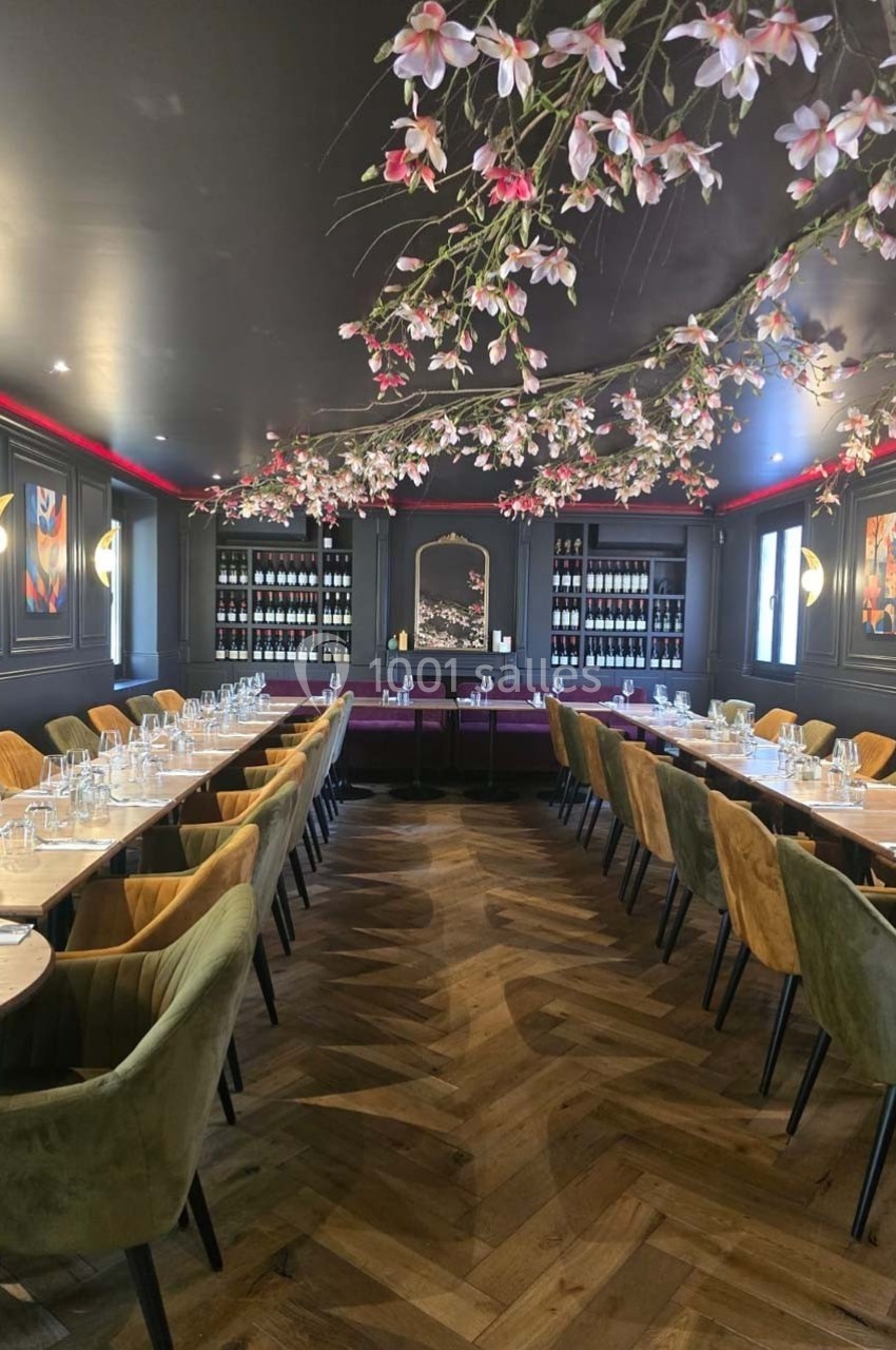Salle de restaurant élégante avec tables dressées, chaises colorées et branches fleuries suspendues au plafond.