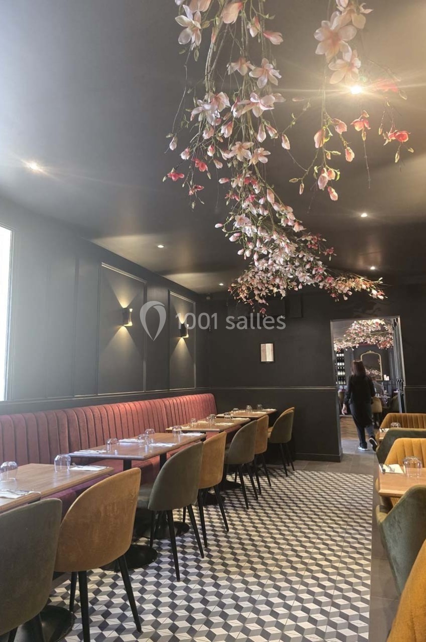 Salle de restaurant élégante avec banquettes rouges, chaises colorées et plafond décoré de fleurs suspendues.