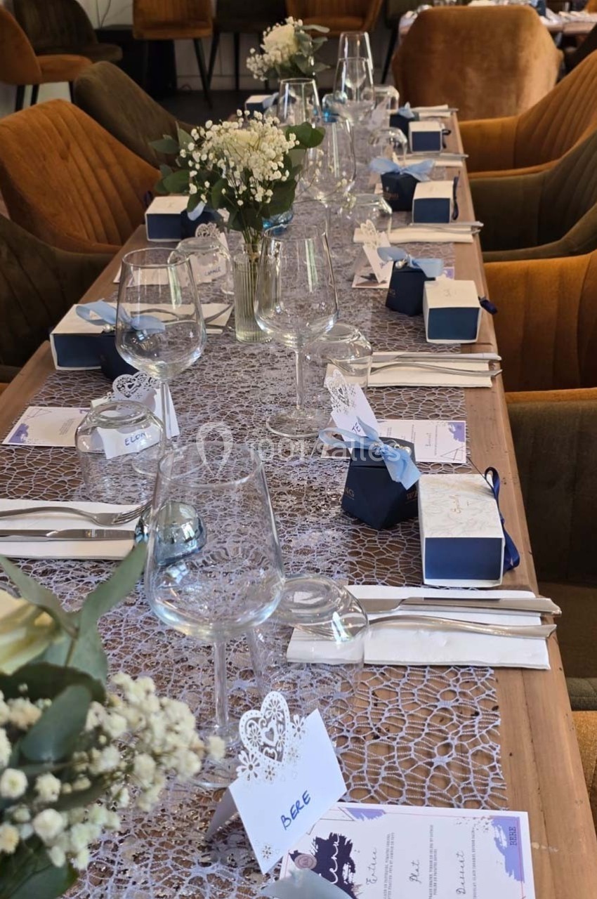 Table dressée pour un repas, ornée de fleurs, cadeaux et menus, avec vaisselle élégante et chaises en velours.