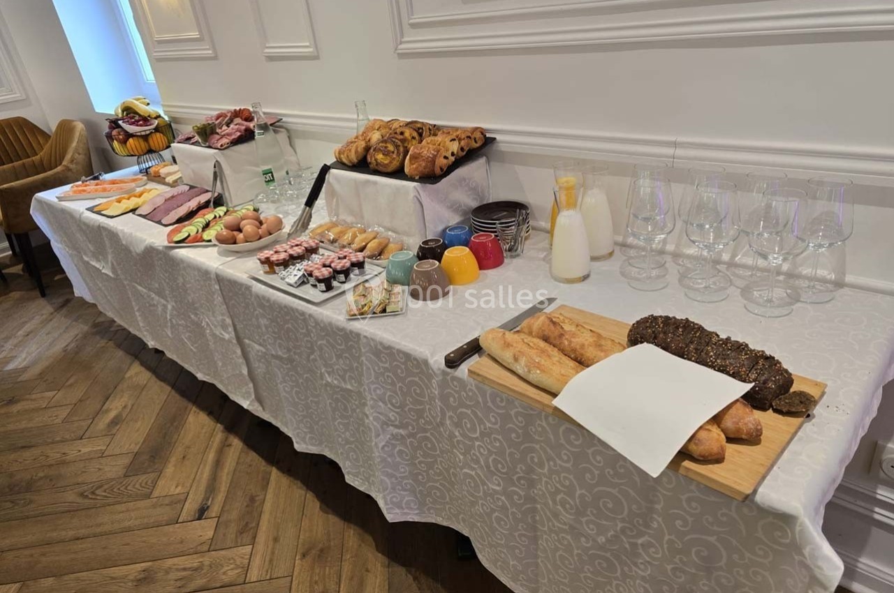 Buffet de petit-déjeuner avec viennoiseries, pains, fruits, charcuteries, œufs, jus et verres disposés sur une table.