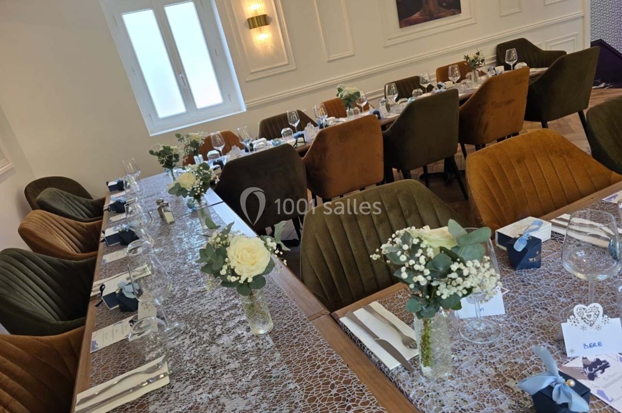 Salle de réception avec tables décorées de nappes en dentelle, fleurs blanches et vaisselle élégante.