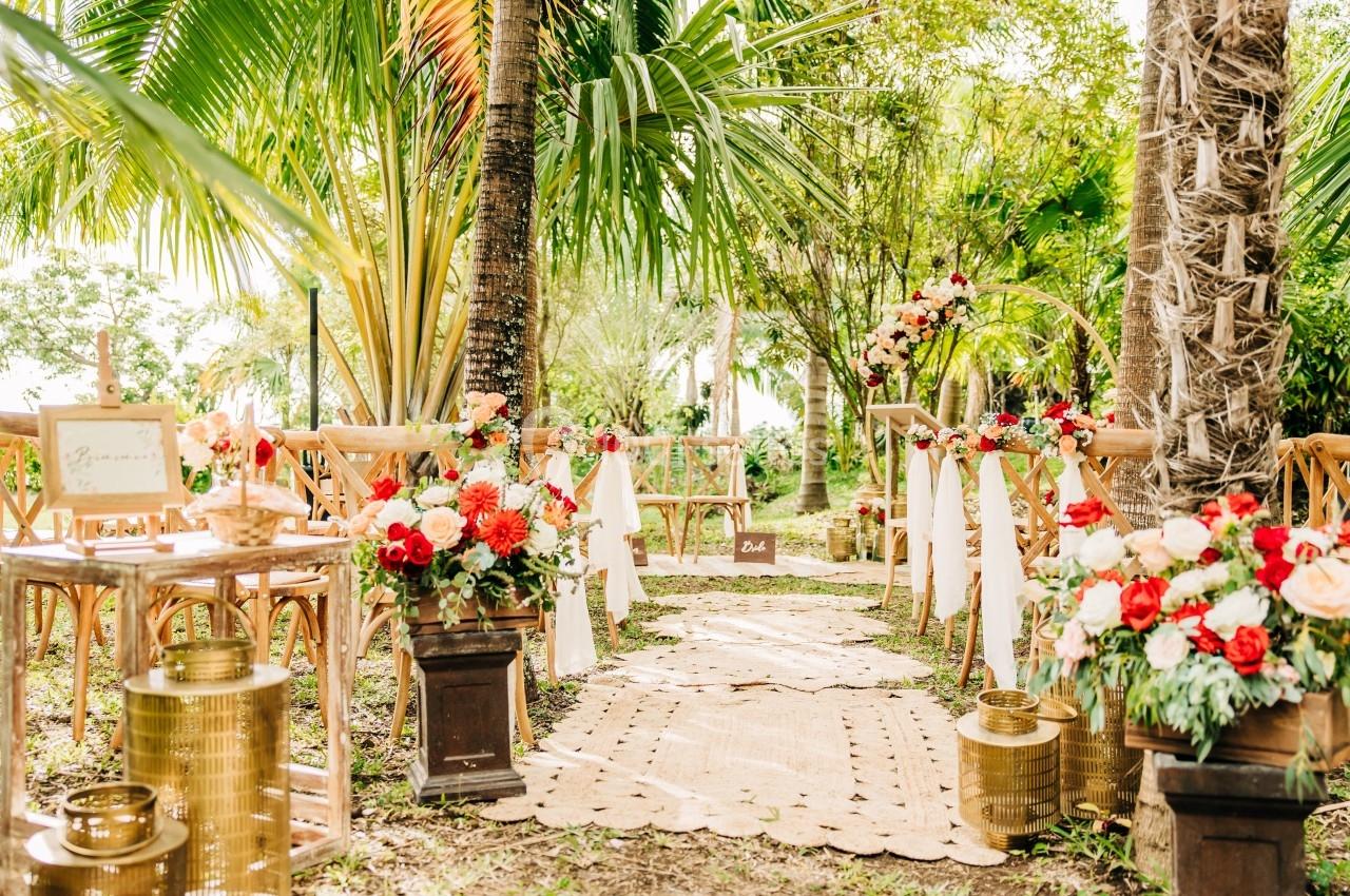 Allée décorée de fleurs colorées et lanternes dorées pour une cérémonie de mariage en plein air, entourée de verdure.