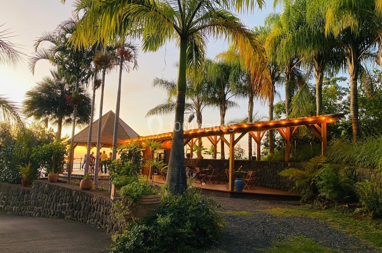 Terrasse en bois éclairée au crépuscule, entourée de palmiers et de végétation tropicale.