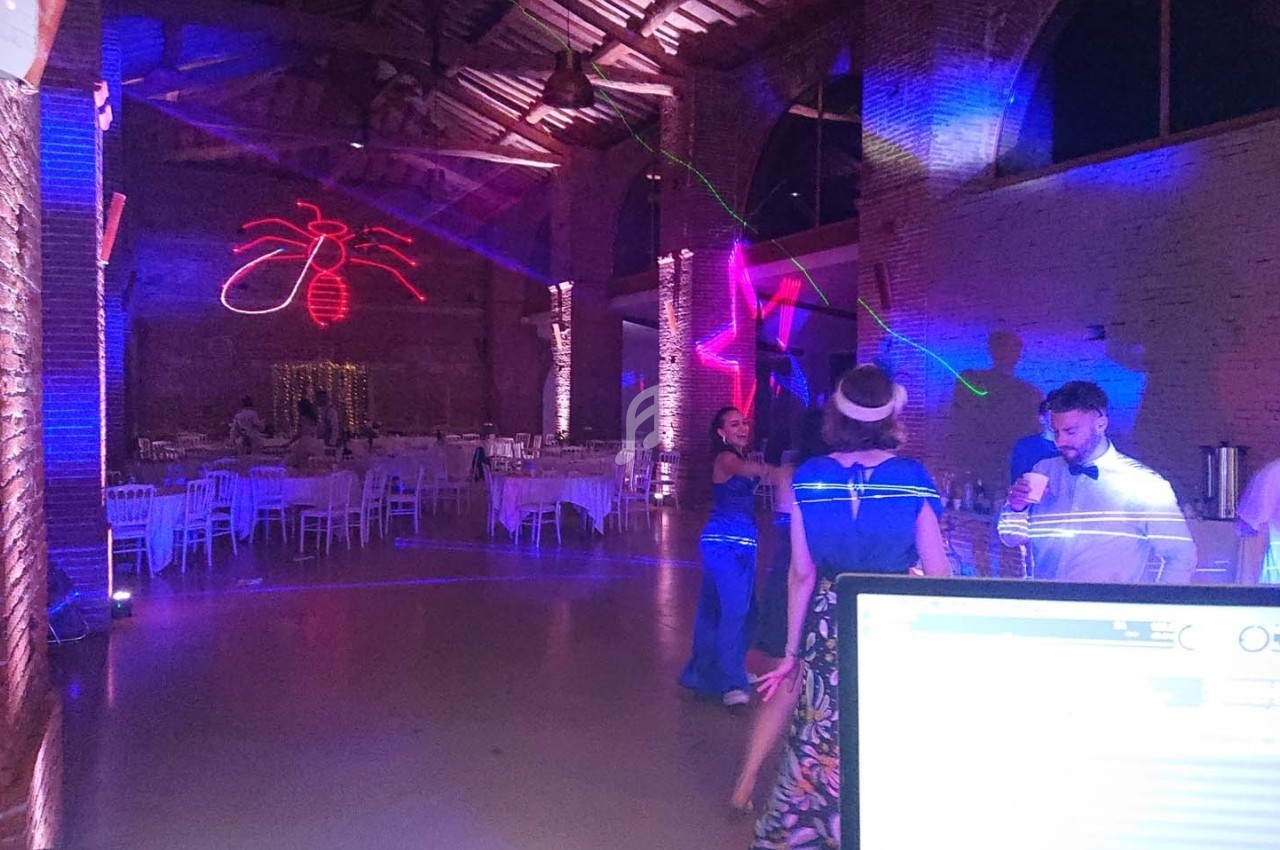 Salle de réception avec éclairages colorés, quelques personnes dansant ou discutant près de tables dressées.