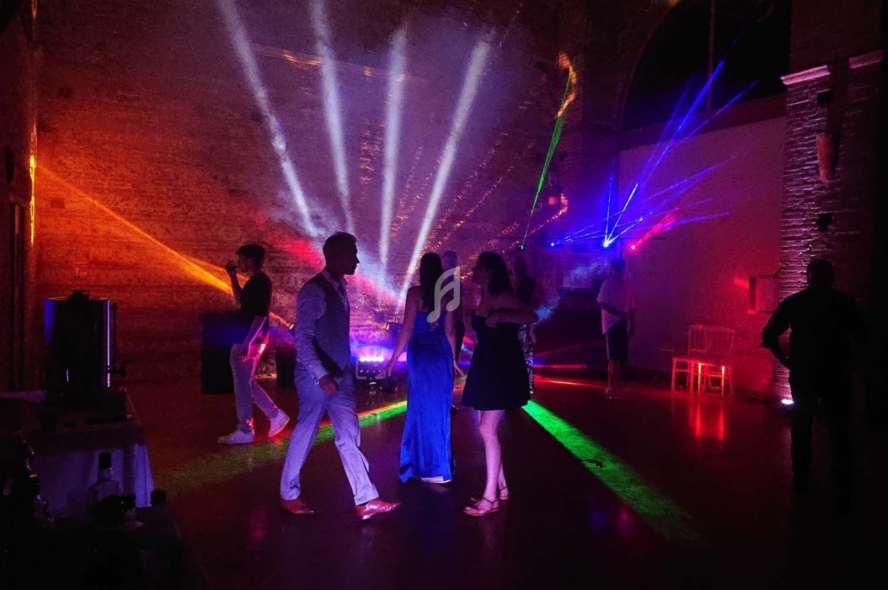 Personnes dansant sous des jeux de lumière colorés dans une salle sombre avec des murs en pierre.
