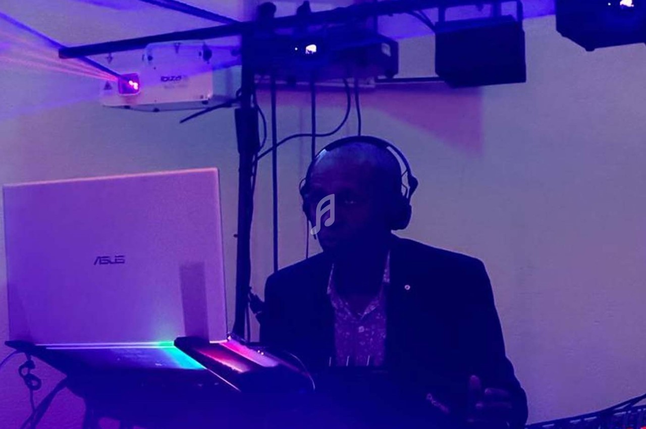 Un DJ portant un casque audio mixe de la musique sur un ordinateur portable dans une ambiance lumineuse tamisée.