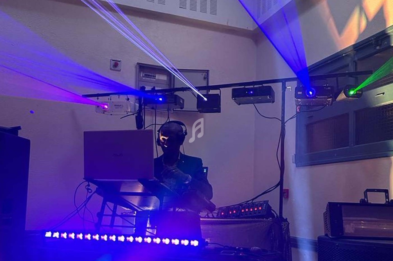 Un DJ mixe dans une salle sombre, éclairée par des faisceaux lumineux colorés et des équipements audio.