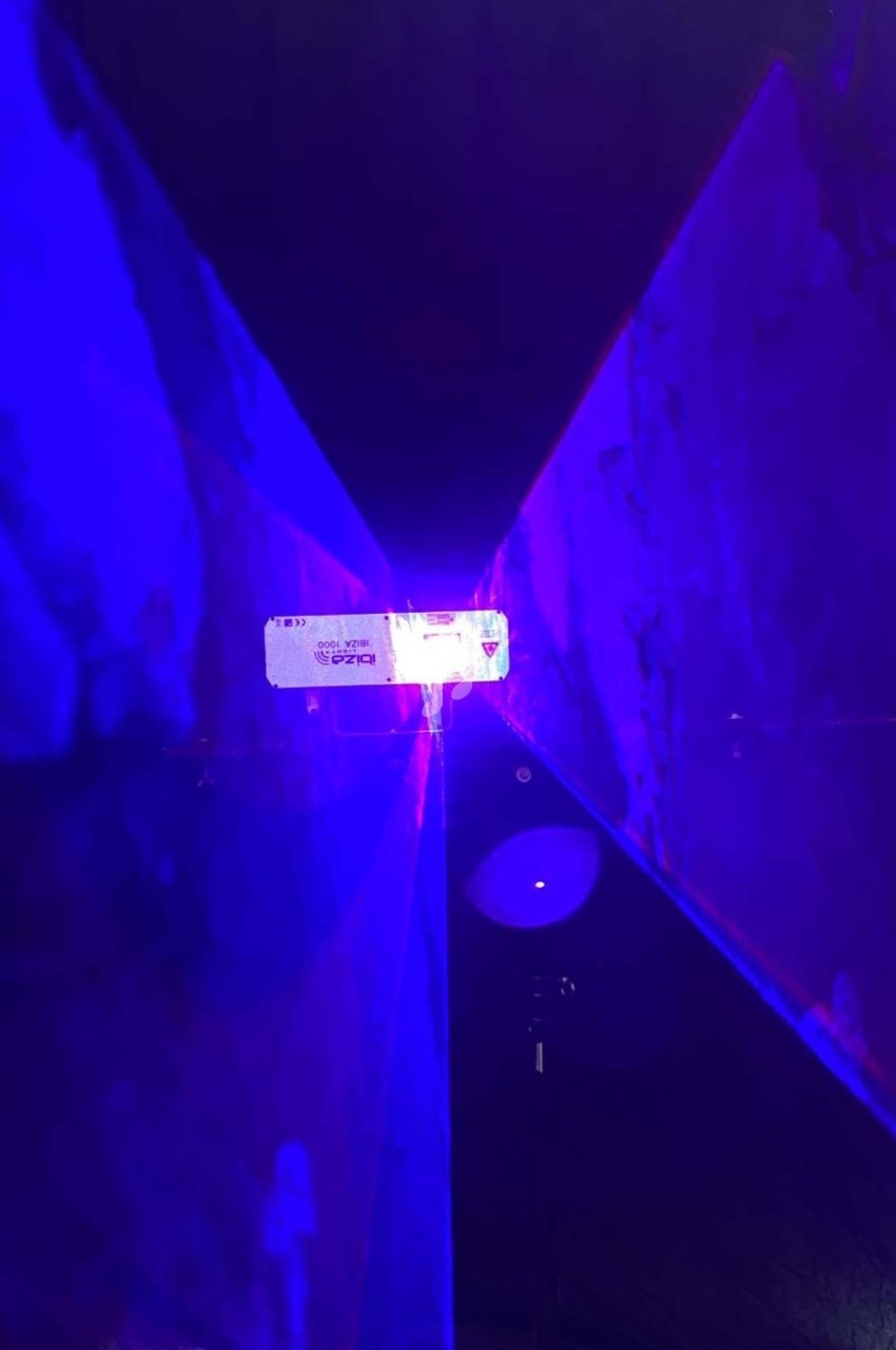 Rayons lumineux violets et bleus se croisant dans un environnement sombre avec un point lumineux central.