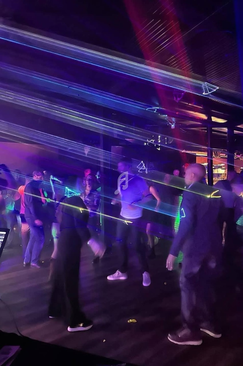 Personnes dansant dans une ambiance sombre avec des lumières laser colorées traversant la salle.