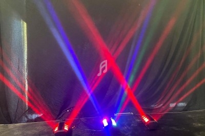 Faisceaux lumineux rouges, bleus et verts projetés en croix sur un fond noir dans un environnement sombre.