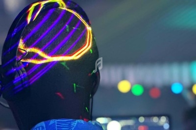 Une personne de dos portant un casque audio, éclairée par des lumières colorées dans un environnement sombre.