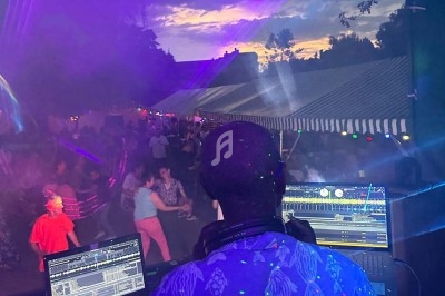 Un DJ mixe en plein air devant une foule dansante sous des tentes éclairées au crépuscule.