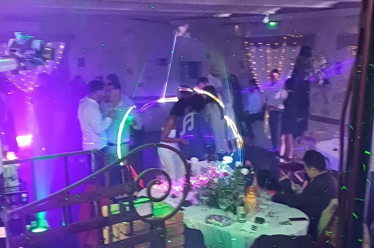 Des invités dansent sous des lumières colorées lors d'une fête, avec des tables décorées en arrière-plan.