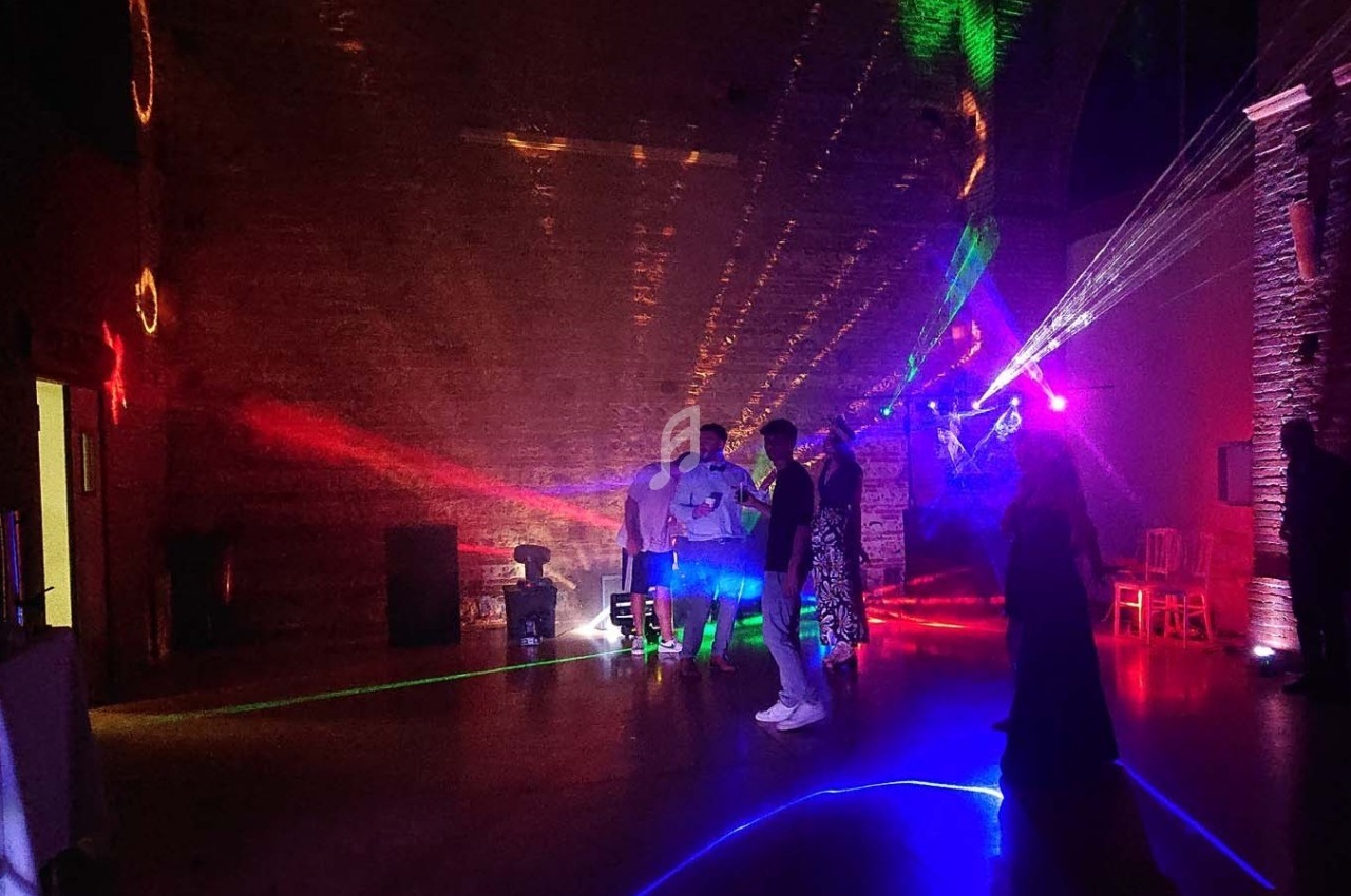 Des personnes discutent dans une salle sombre éclairée par des lumières colorées et des faisceaux laser.