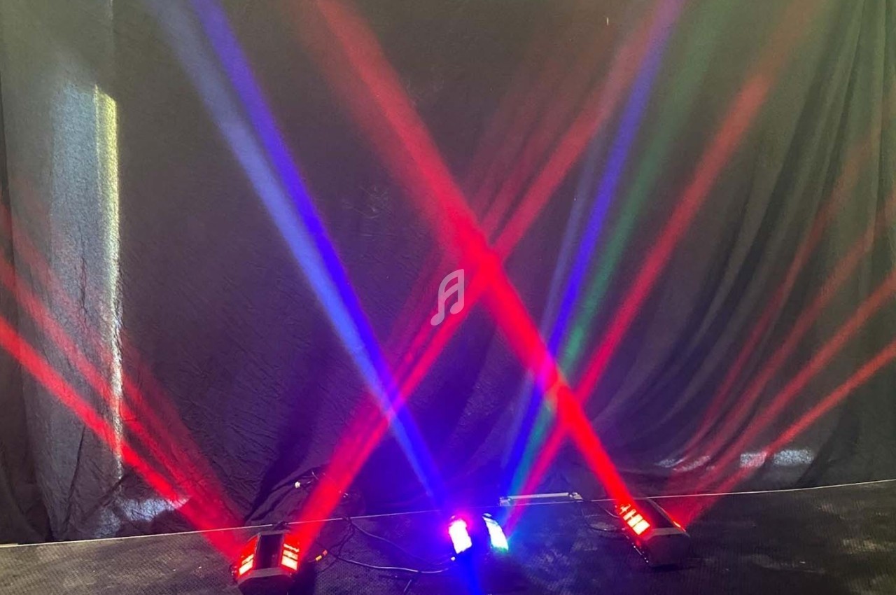 Faisceaux lumineux rouges, bleus et verts projetés en croix sur un fond noir dans un environnement sombre.