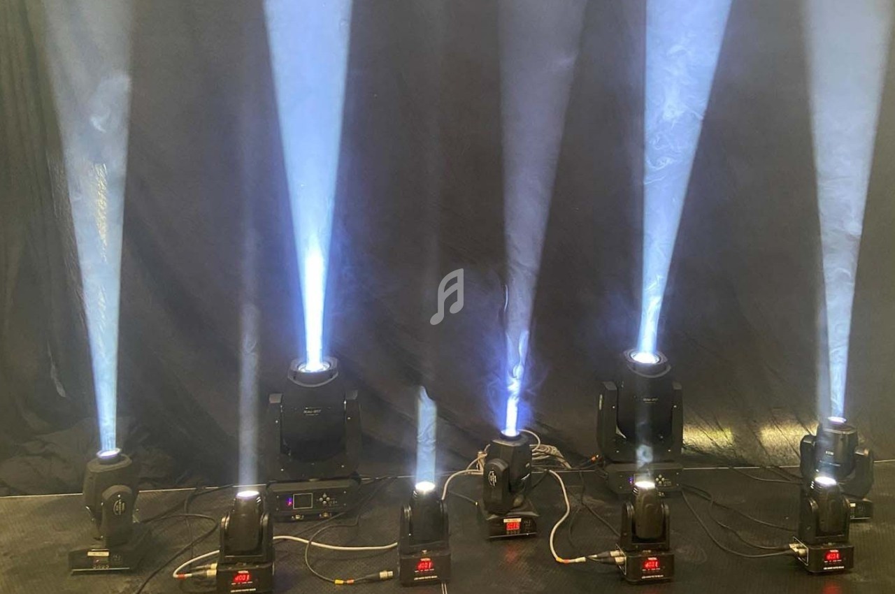 Projecteurs lumineux diffusant des faisceaux blancs sur un fond sombre, alignés sur une scène ou un espace intérieur.