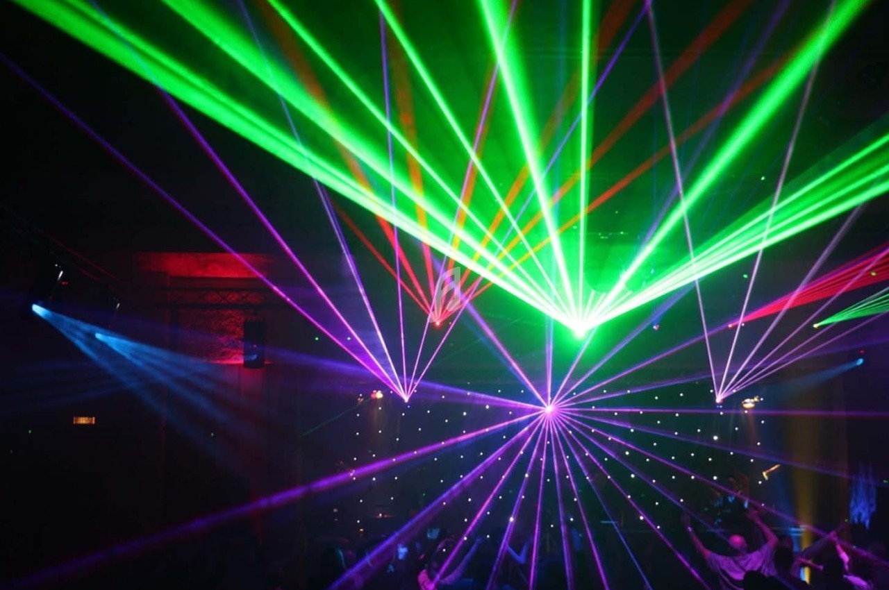 Spectacle de lumières laser multicolores dans une salle sombre avec des faisceaux verts, rouges et violets.