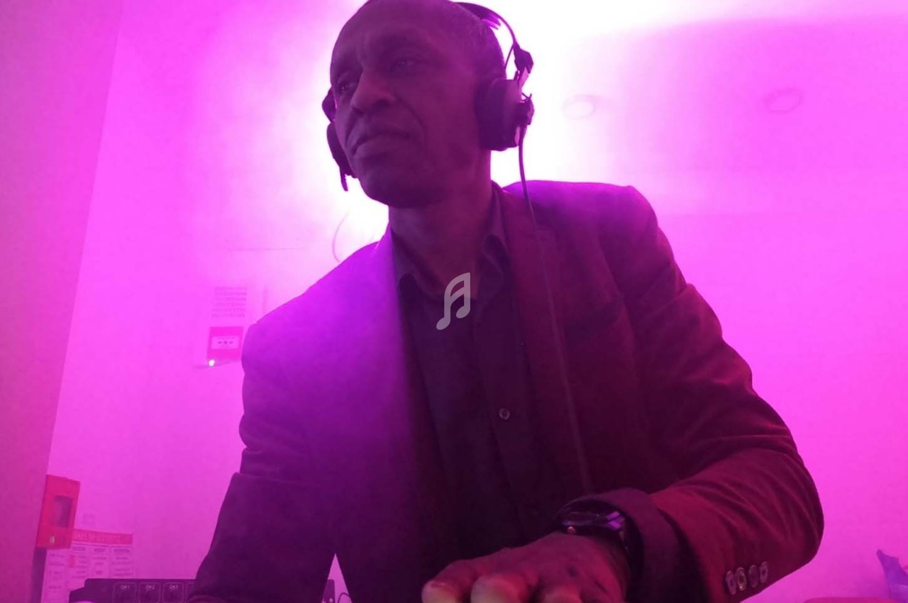 Homme portant un casque audio, debout dans une ambiance lumineuse rose, semblant manipuler un équipement.