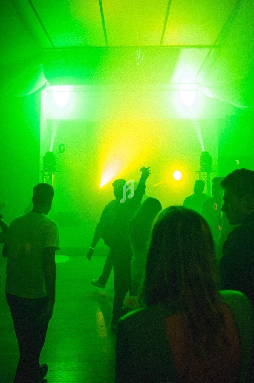 Personnes dansant dans une salle éclairée par des lumières vertes et jaunes, créant une ambiance festive.