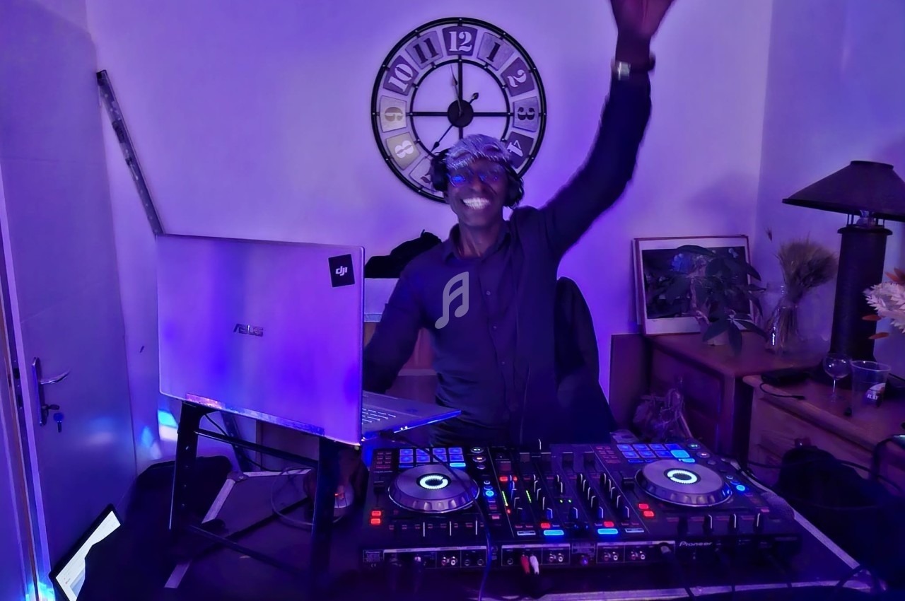 Un DJ souriant mixe de la musique sur une table de mixage dans une pièce éclairée par des lumières colorées.