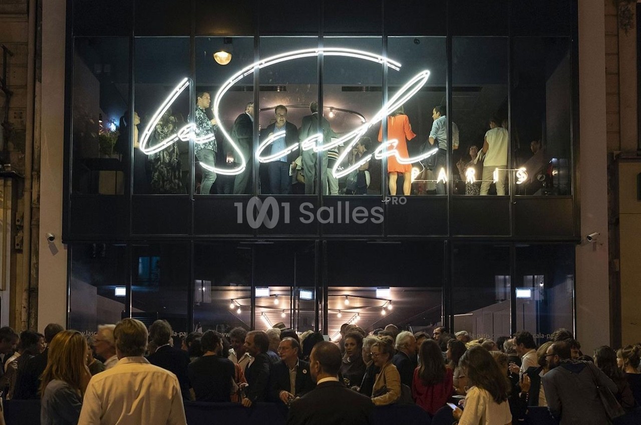 Foule rassemblée devant une façade vitrée illuminée avec le logo ’La Scala Paris’ visible à l'étage supérieur.