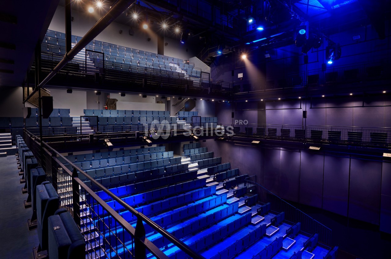 Salle de théâtre moderne avec sièges bleus, éclairage tamisé et projecteurs suspendus au plafond.