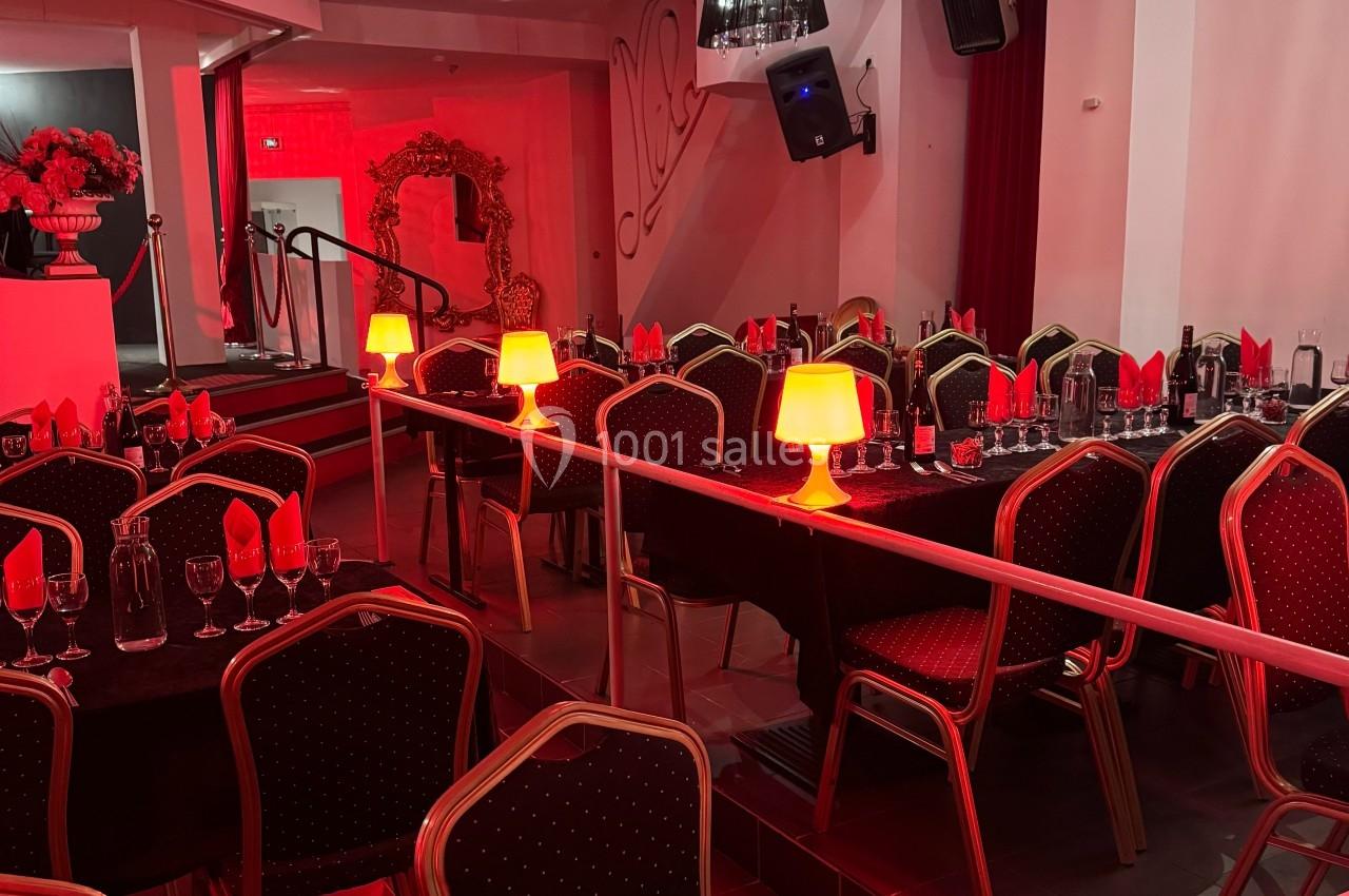 Salle de réception décorée avec des tables dressées, nappes noires, serviettes rouges et lampes d'ambiance rouges.
