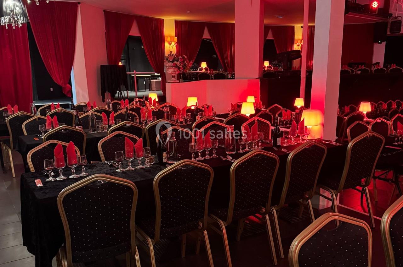 Salle de réception avec tables dressées, nappes noires, serviettes rouges et lampes d'ambiance rouge.
