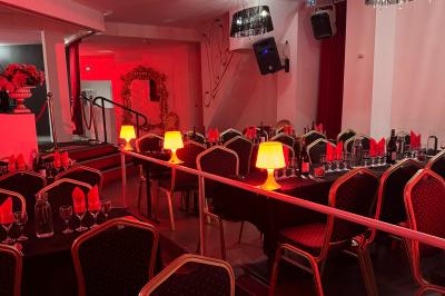 Salle décorée avec des rideaux rouges, tables dressées avec chaises noires et dorées, ambiance tamisée.