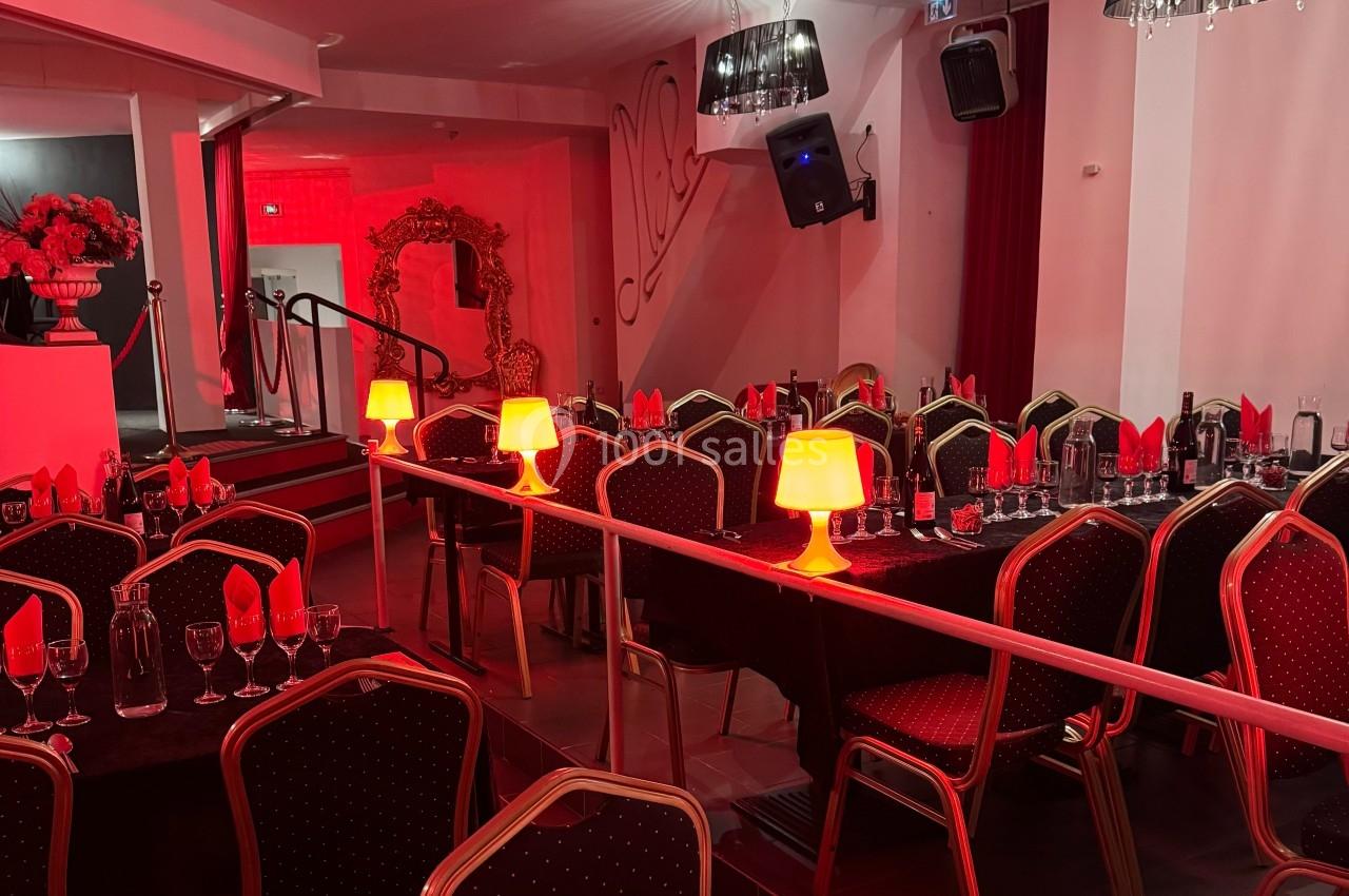 Salle de réception avec tables dressées, nappes noires, serviettes rouges et lampes d'ambiance diffusant une lumière chaude.