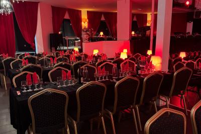 Salle décorée avec des rideaux rouges, tables dressées avec chaises noires et dorées, ambiance tamisée.