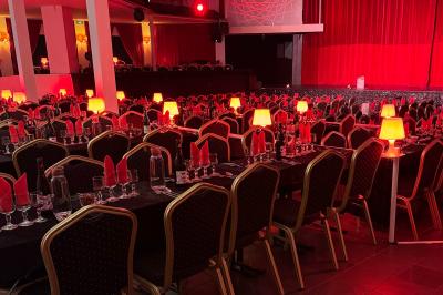 Salle décorée avec des rideaux rouges, tables dressées avec chaises noires et dorées, ambiance tamisée.