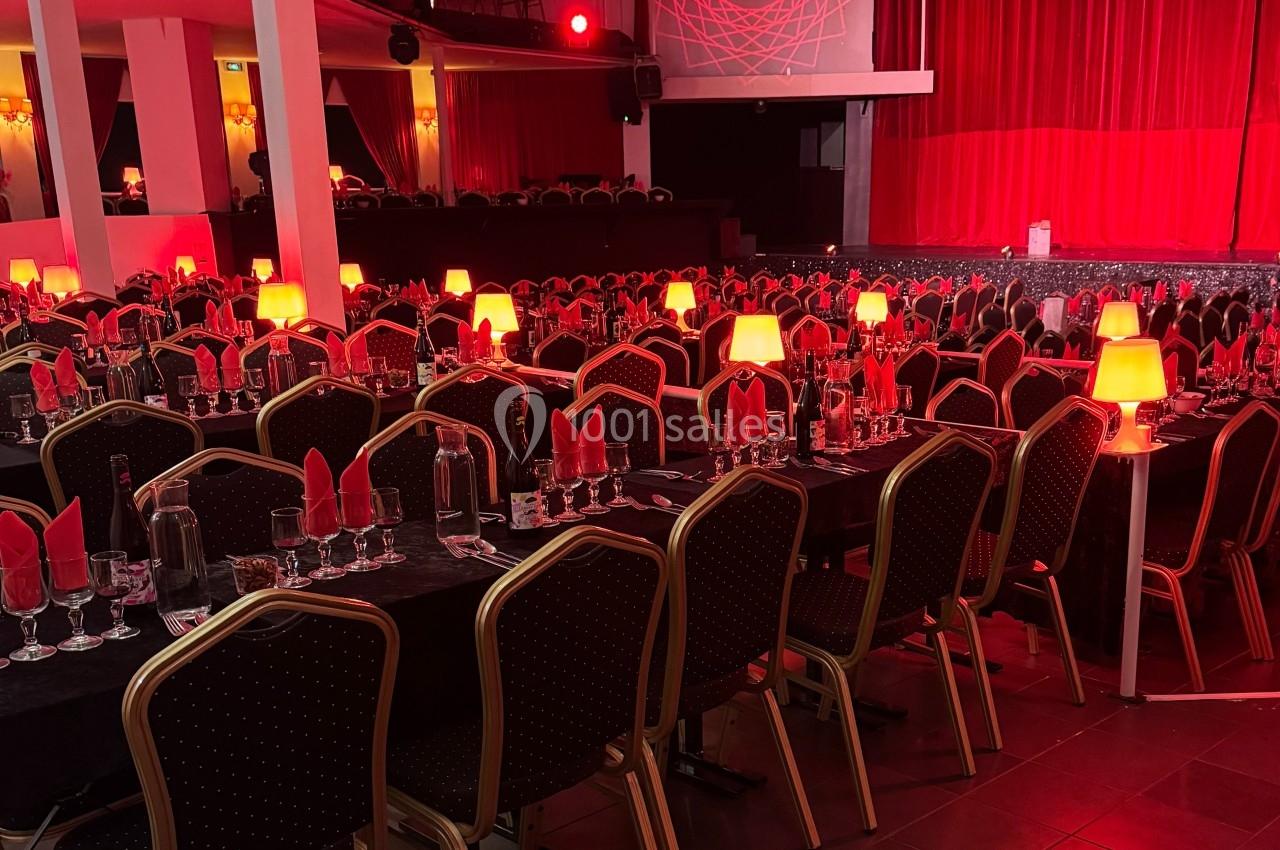 Salle de réception avec tables dressées, nappes noires, serviettes rouges et petites lampes éclairant l'ambiance.