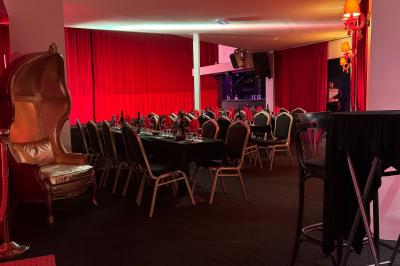 Salle décorée avec des rideaux rouges, tables dressées avec chaises noires et dorées, ambiance tamisée.