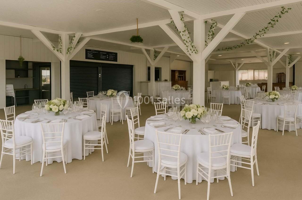 Salle de réception lumineuse avec des tables rondes dressées, décorées de nappes blanches et de bouquets floraux.