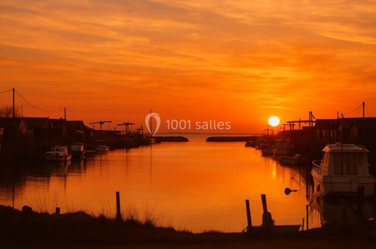 Coucher de soleil sur un port calme, avec des bateaux amarrés et des cabanes en bois bordant l'eau.