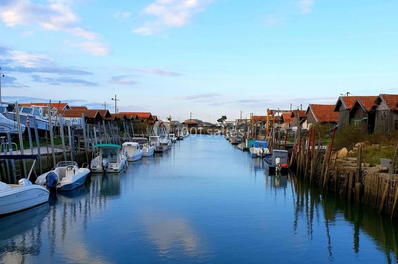 Canal bordé de cabanes en bois et de bateaux amarrés, sous un ciel partiellement nuageux.