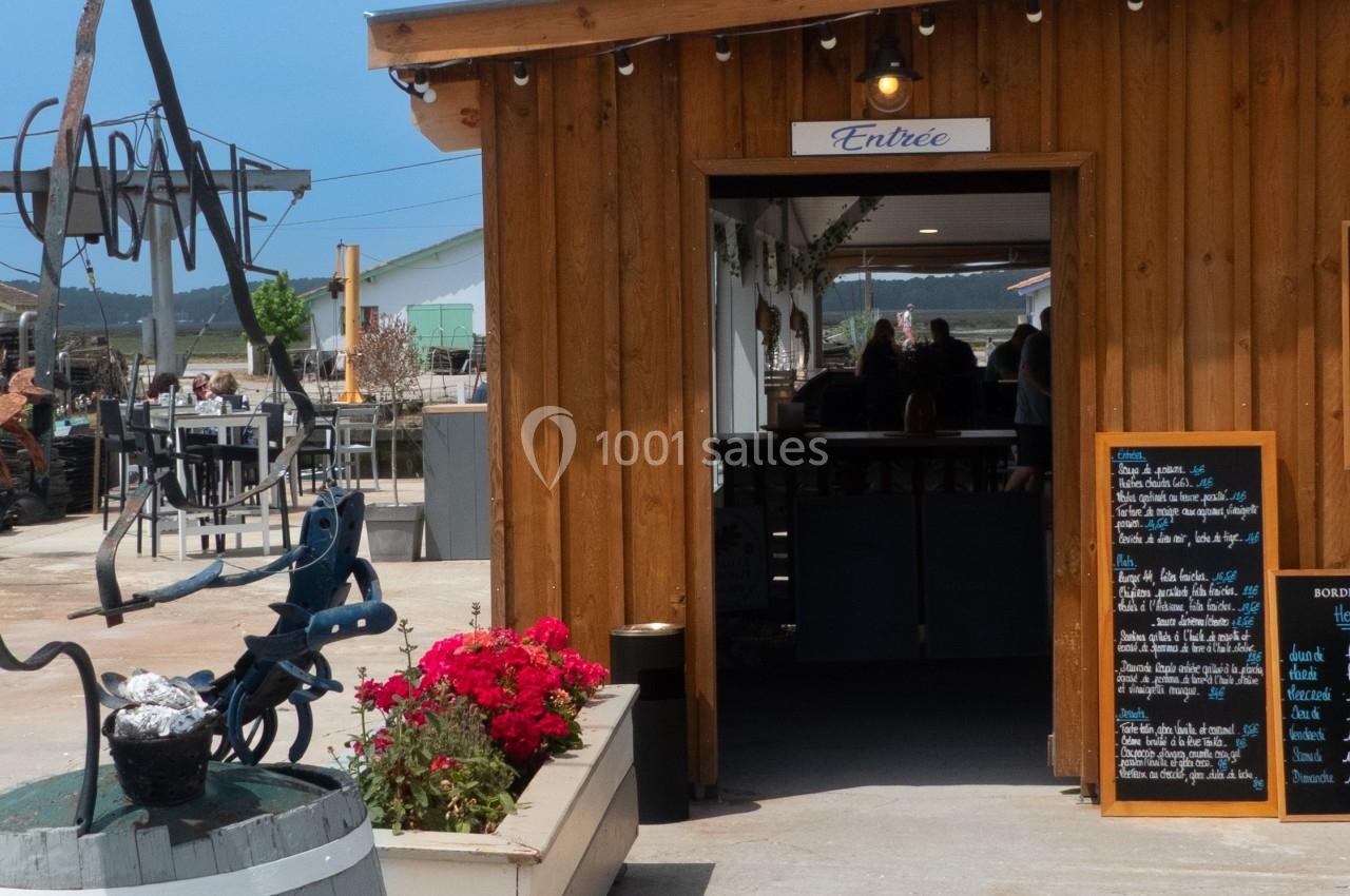 Entrée d'une cabane en bois avec terrasse extérieure, panneau d'affichage et jardinière fleurie au premier plan.