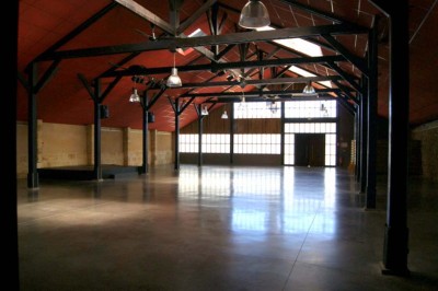 Intérieur d'un grand hangar vide avec charpente en bois, sol en béton poli et lumière naturelle entrant par de larges…