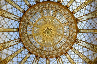 Lustre en cristal doré suspendu sous un plafond peint avec des nuances pastel de bleu et de rose.
