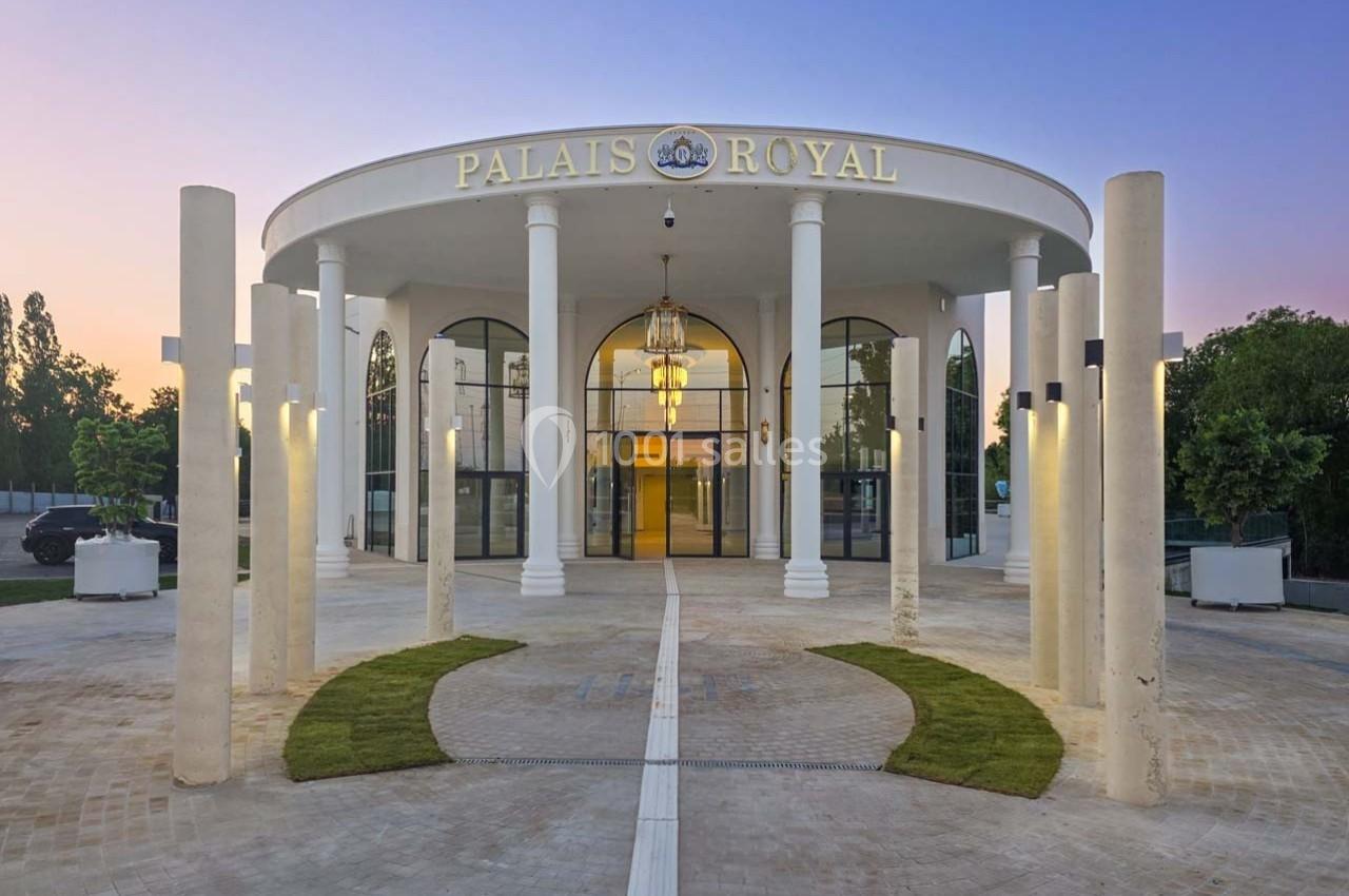 Façade d'un bâtiment circulaire avec colonnes blanches, enseigne ’Palais Royal’ et éclairage au crépuscule.