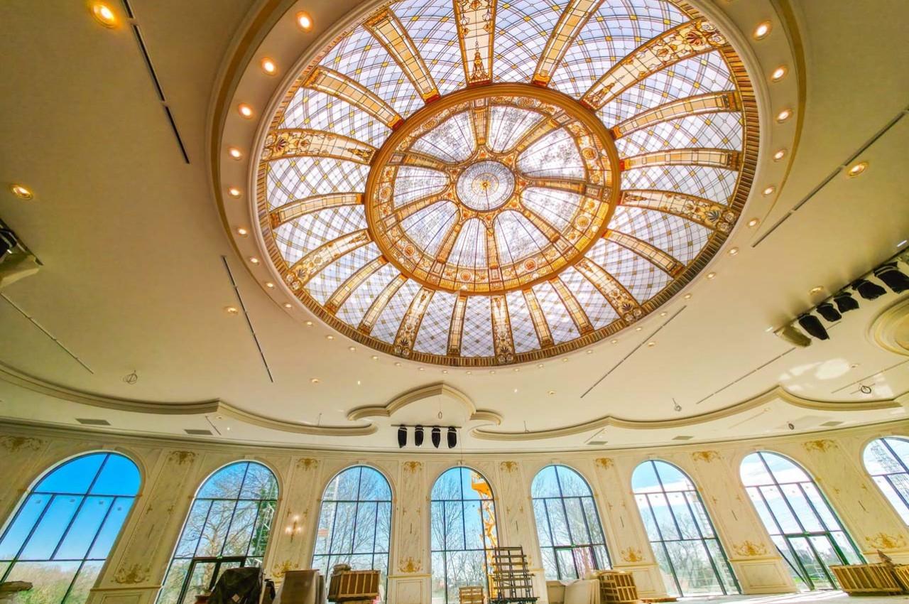 Plafond en dôme avec verrière ornée de motifs dorés, entouré de grandes fenêtres laissant entrer la lumière naturelle.