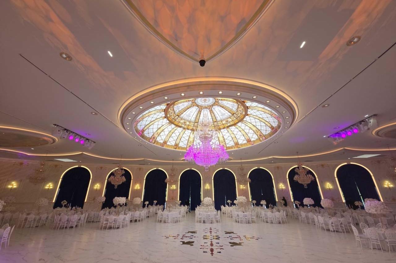 Salle de réception élégante avec un plafond en dôme vitré, un grand lustre central et des tables décorées.