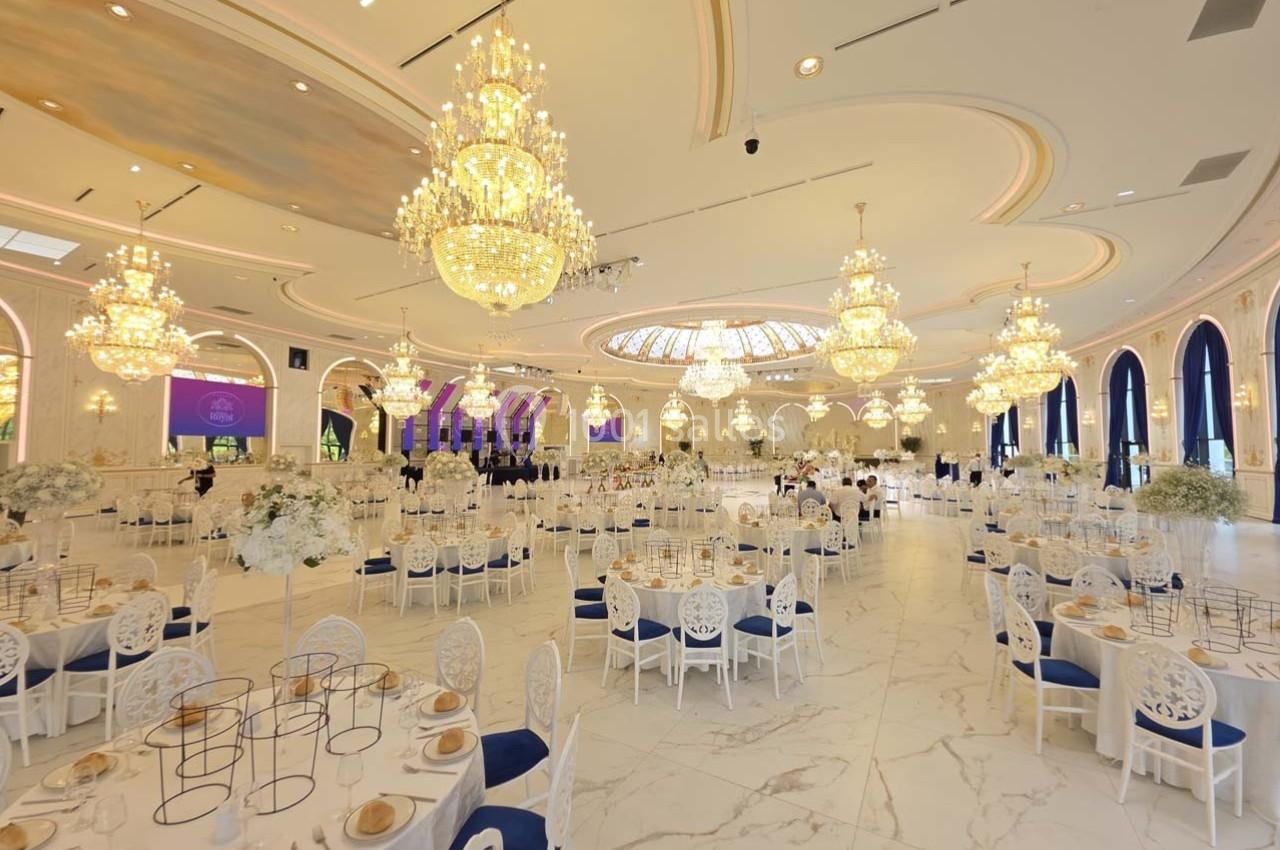 Salle de réception élégante avec lustres imposants, tables dressées et décorations florales blanches.