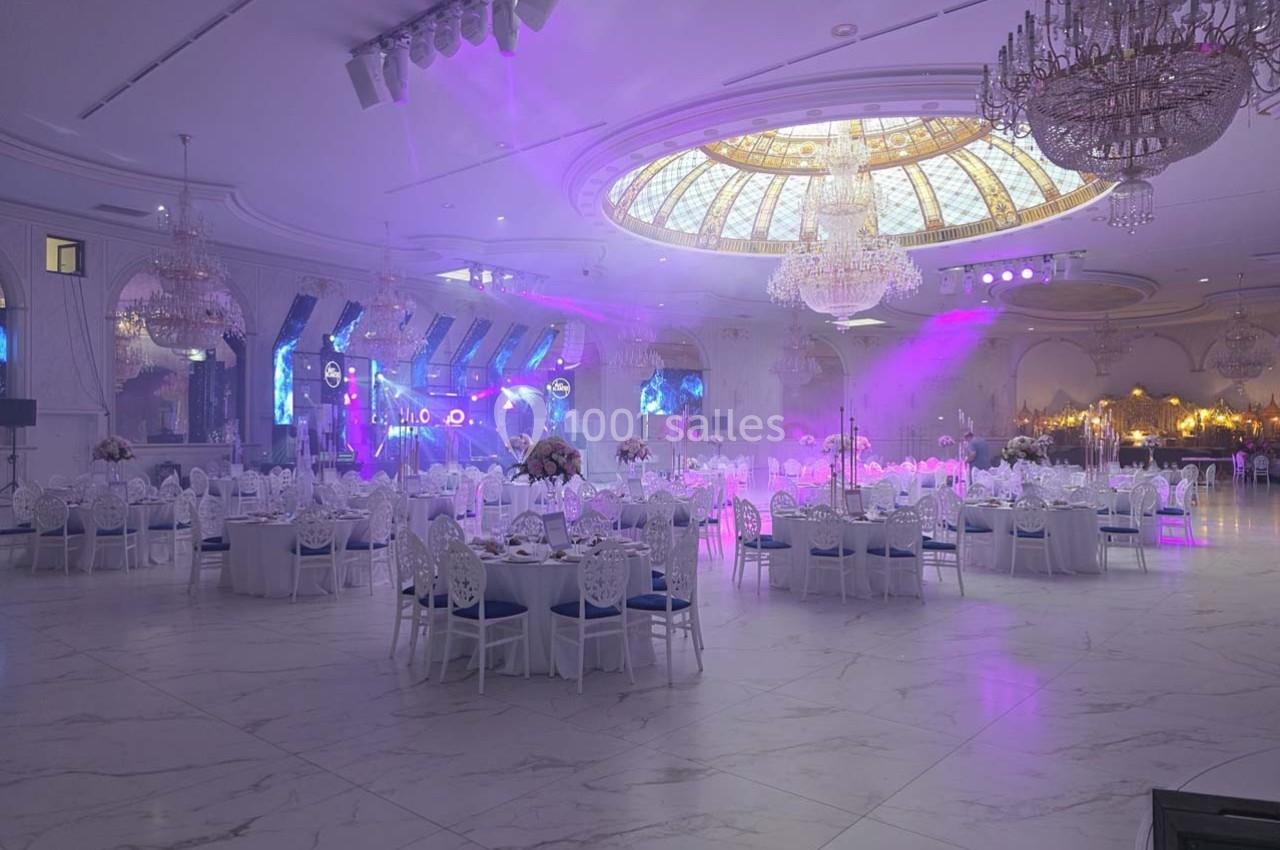 Salle de réception élégante avec tables dressées, lustres imposants et éclairage coloré créant une ambiance festive.
