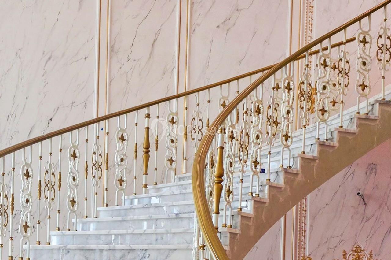 Escalier en marbre blanc avec une rampe ornée de motifs dorés, dans un intérieur aux murs clairs et élégants.