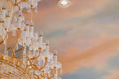 Lustre en cristal doré suspendu sous un plafond peint avec des nuances pastel de bleu et de rose.