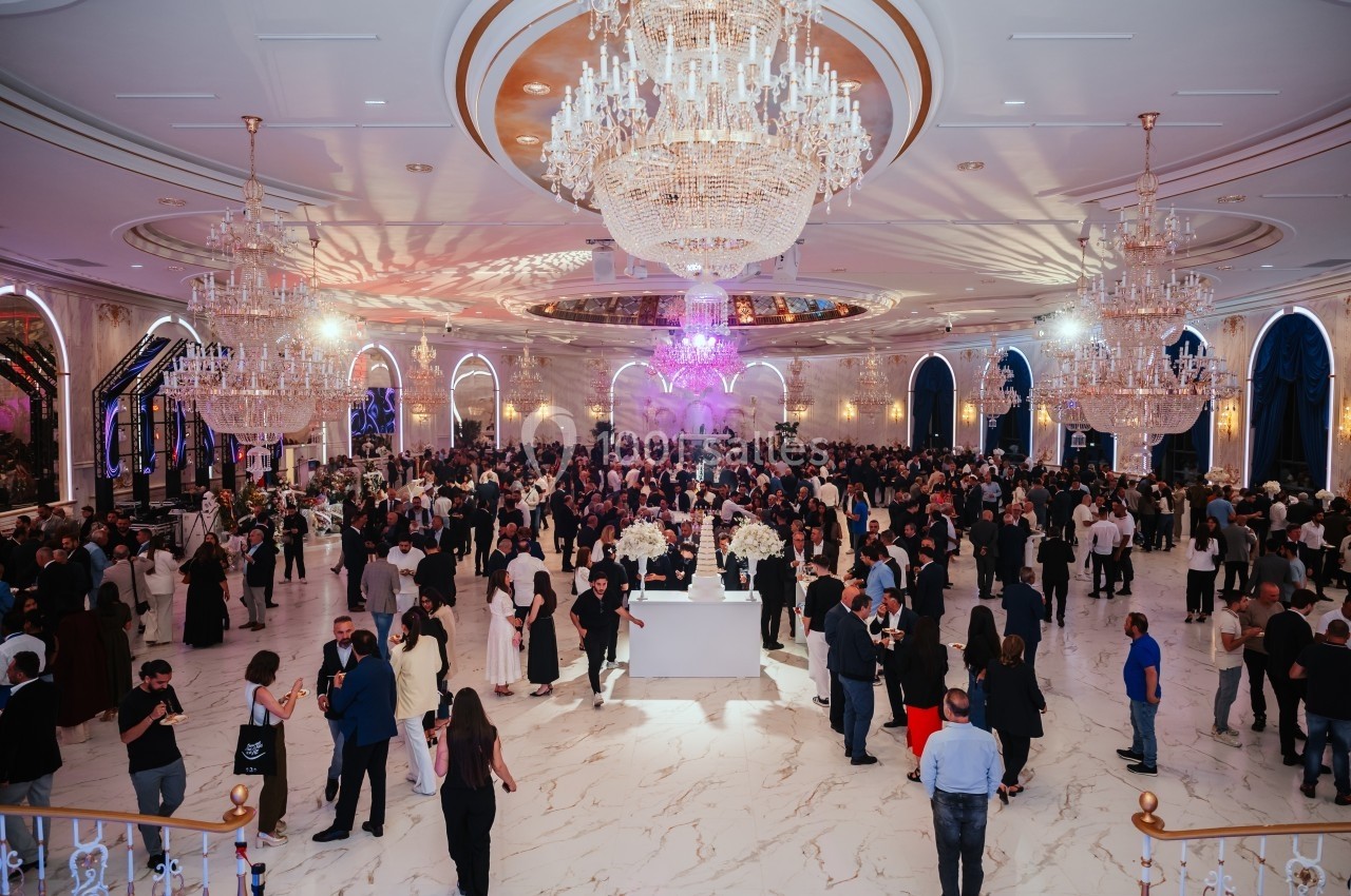 Salle de réception élégante avec de grands lustres, des invités rassemblés et une décoration lumineuse.