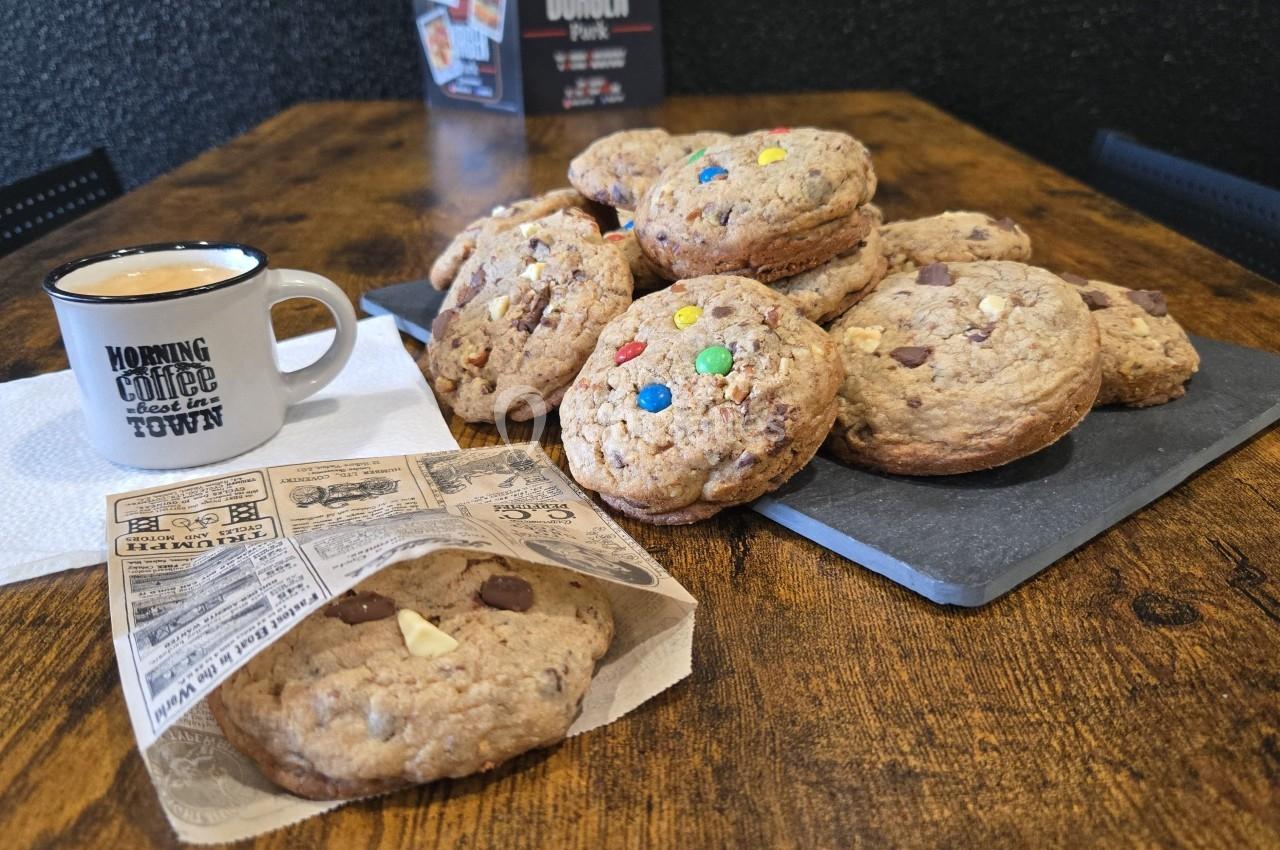 Assortiment de cookies aux pépites de chocolat et bonbons colorés sur une table en bois, avec une tasse de café.